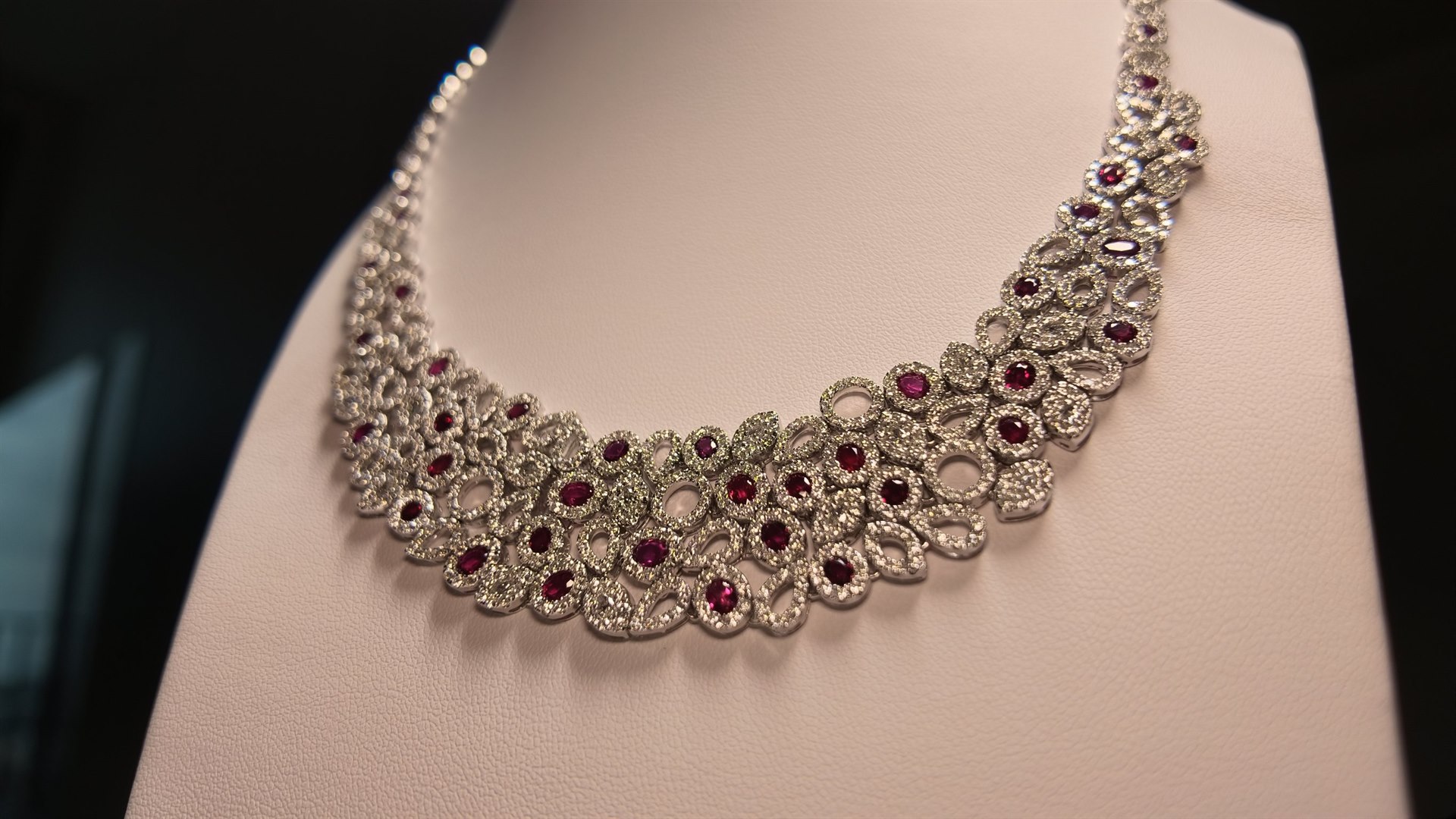 A ruby and diamond collar necklace resting on a white display bust, its tapered ends set with graduated rubies.